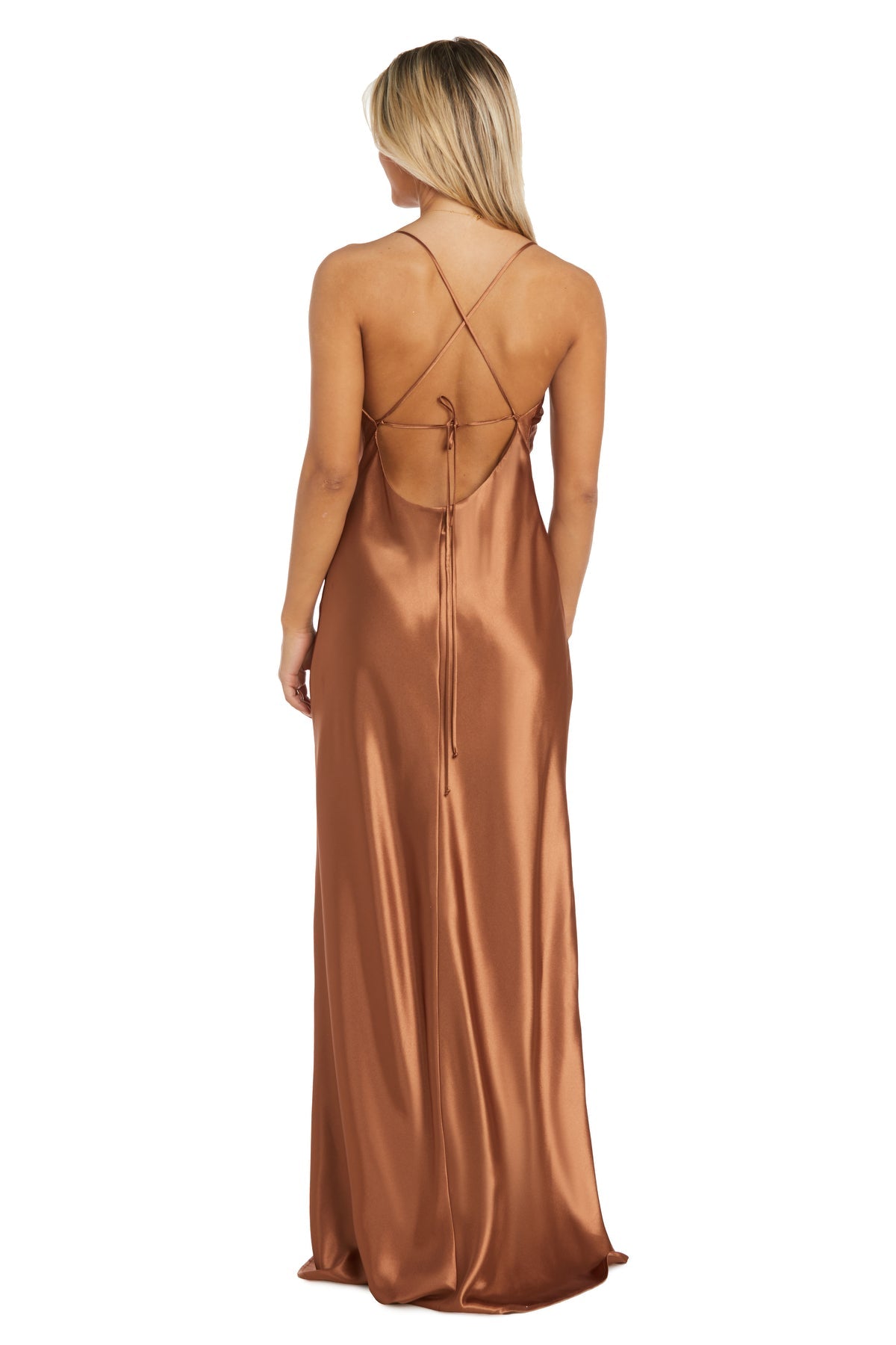 A woman stands facing away, wearing the Morgan 10037N cowl-neck long satin prom dress featuring thin cross-back straps and a dramatic open back in shiny copper.